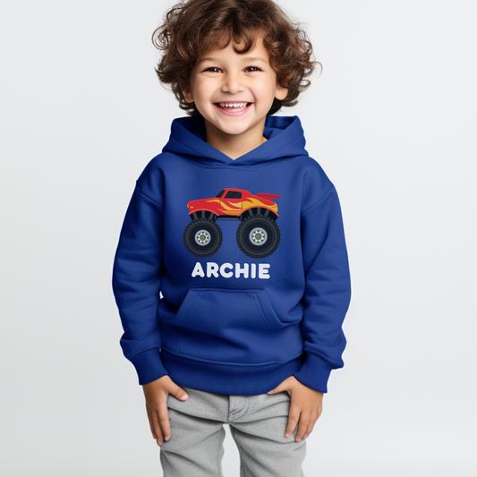 A little boy wearing a blue hoodie with a printed monster truck design and personalised name in white