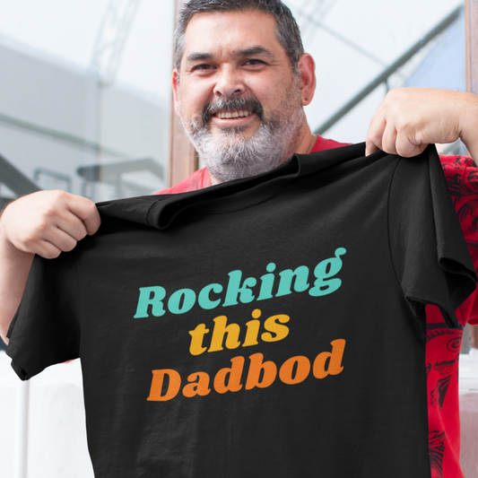 Smiling man holding a black “Rocking This Dadbod” slogan t-shirt with colourful text design