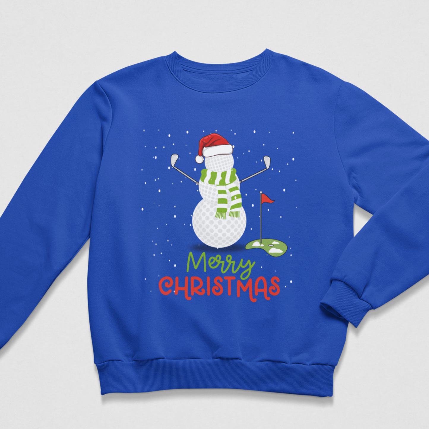 A royal blue crewneck sweatshirt featuring a Christmas-themed golf graphic. The design shows a snowman wearing a red Santa hat and green striped scarf, holding golf clubs near a green hole with a red flag, above the text 'Merry Christmas' in green and red.