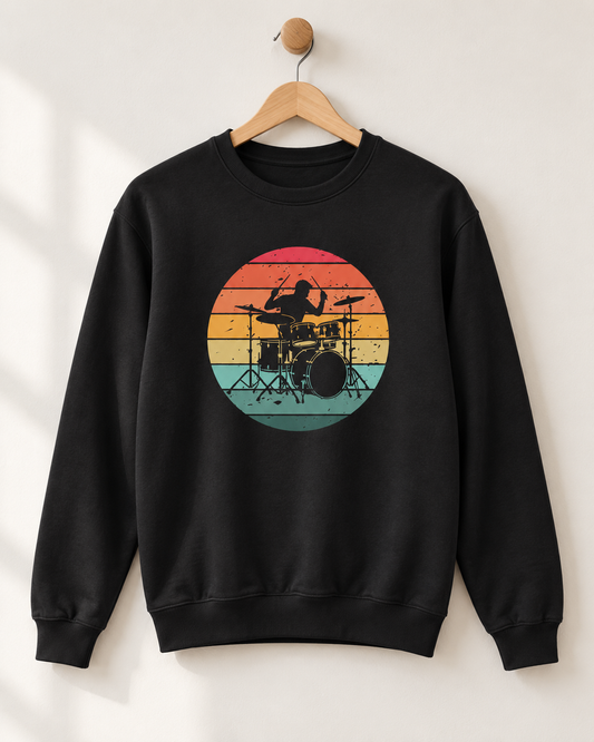 Black adult sweatshirt hanging from a wooden wall hook, featuring a drummer and drum kit silhouette against colourful distressed sunset stripes.