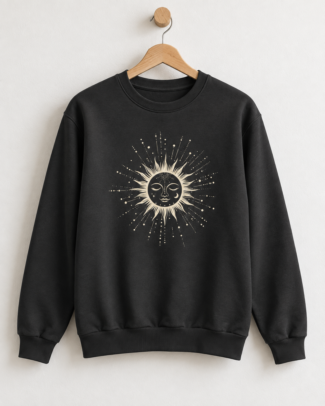 Jet black unisex sweatshirt hanging on a wooden hanger with a central celestial sun face print surrounded by intricate sunburst rays and stars
