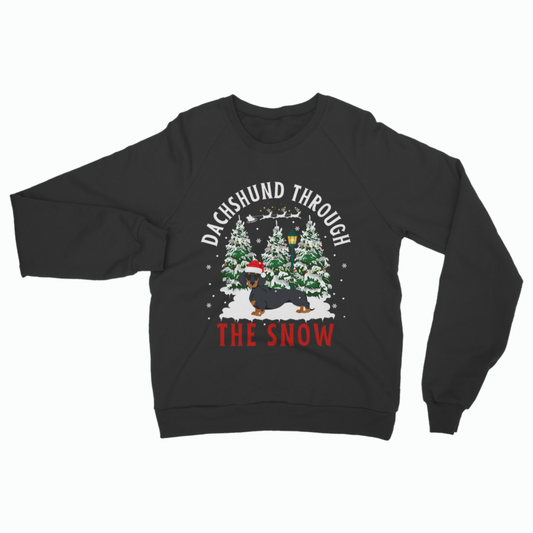 A black crewneck sweatshirt featuring a festive Christmas graphic with the text 'DACHSHUND THROUGH THE SNOW'. The graphic depicts a black dachshund wearing a red Santa hat, walking through snow-covered pine trees with a sleigh and Santa in the sky.