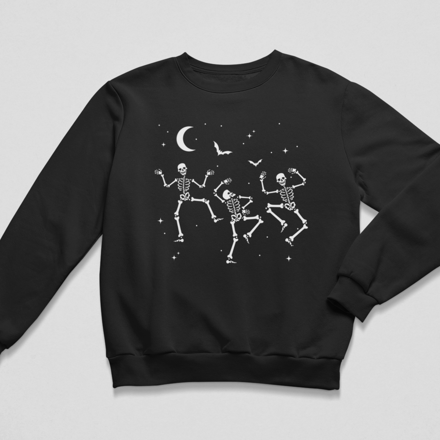 Black unisex Halloween sweatshirt featuring three white dancing skeletons beneath bats and a crescent moon.