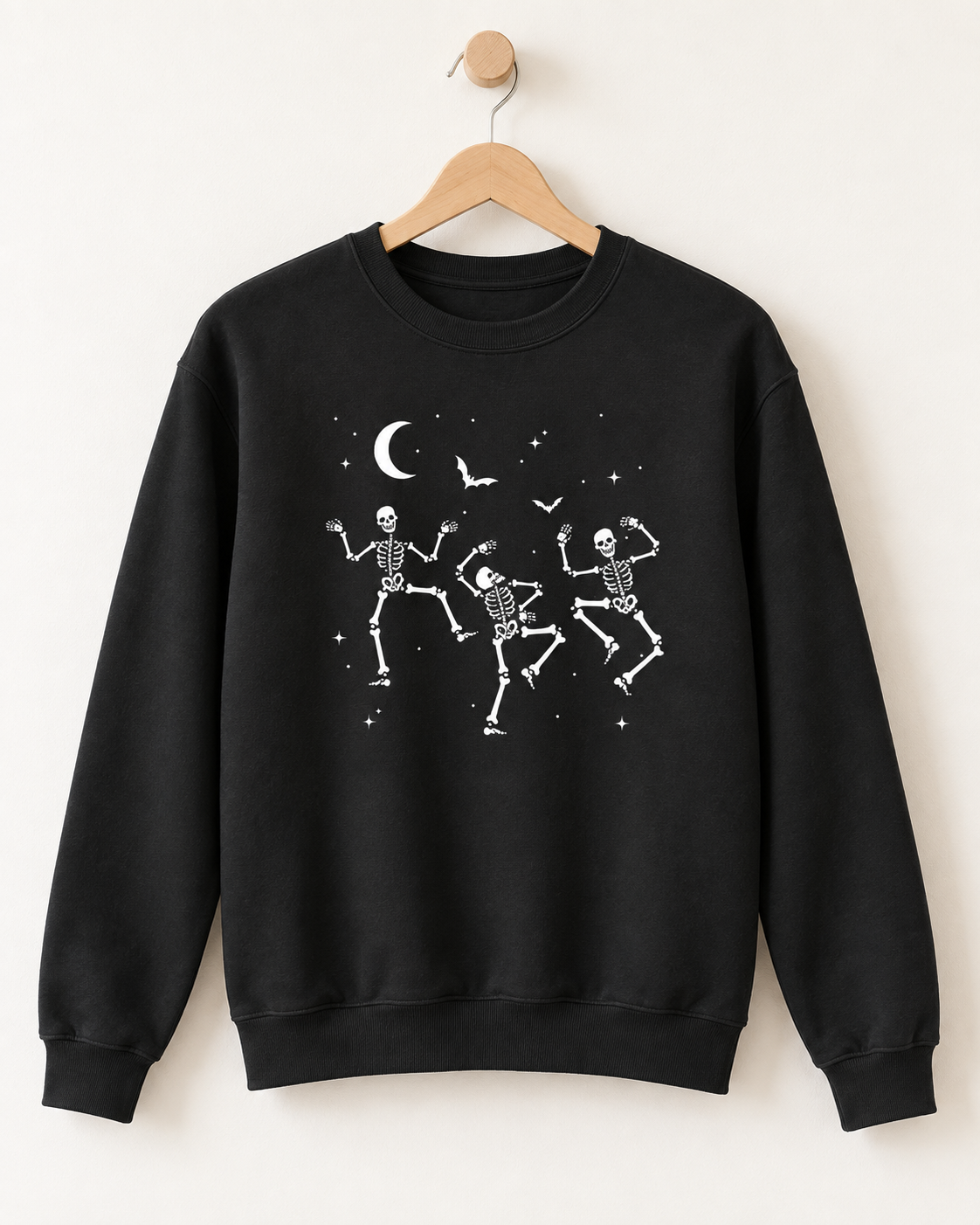 Black adult Halloween sweatshirt with three dancing skeletons, bats and crescent moon displayed on a wooden hanger.