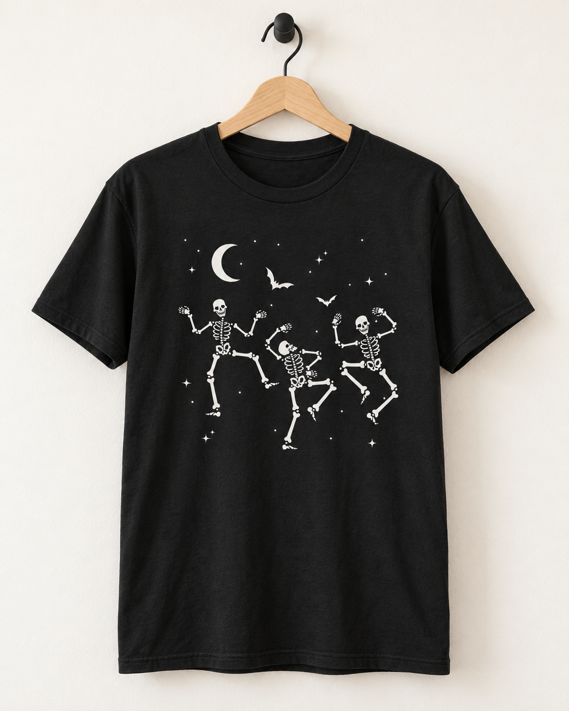 Black dancing skeletons Halloween T-shirt displayed on a wooden hanger and matte-black wall hook.