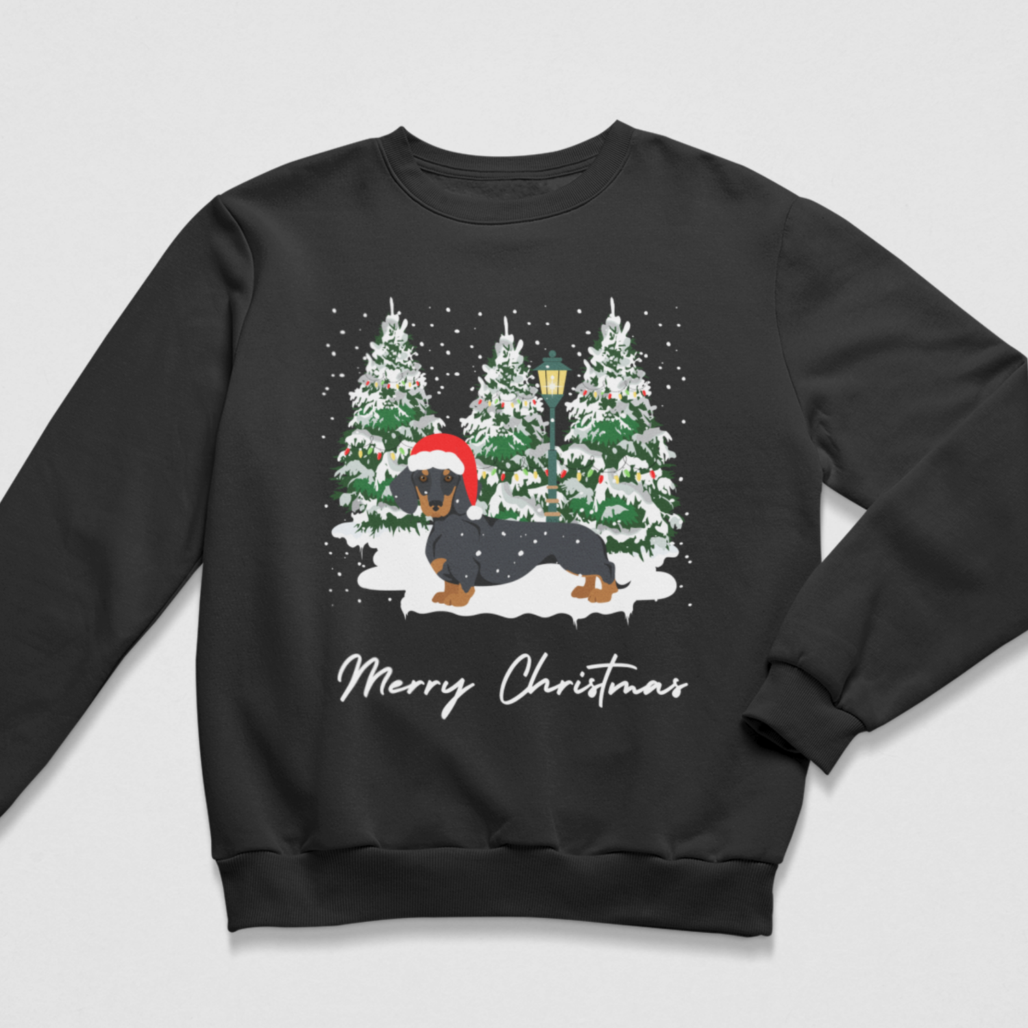 A black crewneck sweatshirt featuring a festive Christmas graphic of a dachshund wearing a Santa hat in the snow, with three decorated Christmas trees and the text 'Merry Christmas' printed below.