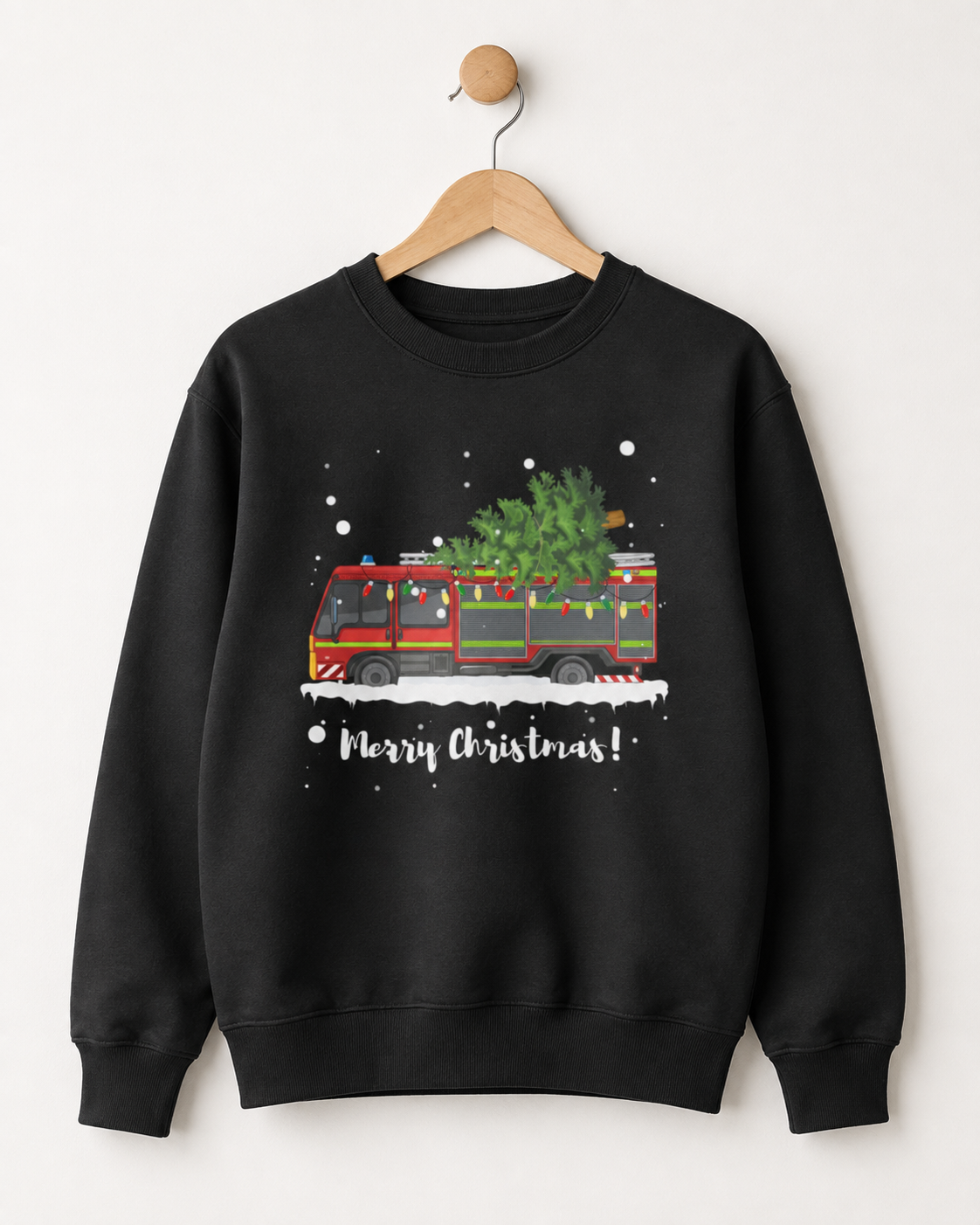 A black crewneck sweatshirt hanging on a wooden hanger against a light beige wall. The sweatshirt features a graphic of a red fire truck carrying a green Christmas tree, with white snowflakes and the text 'Merry Christmas!' printed below.