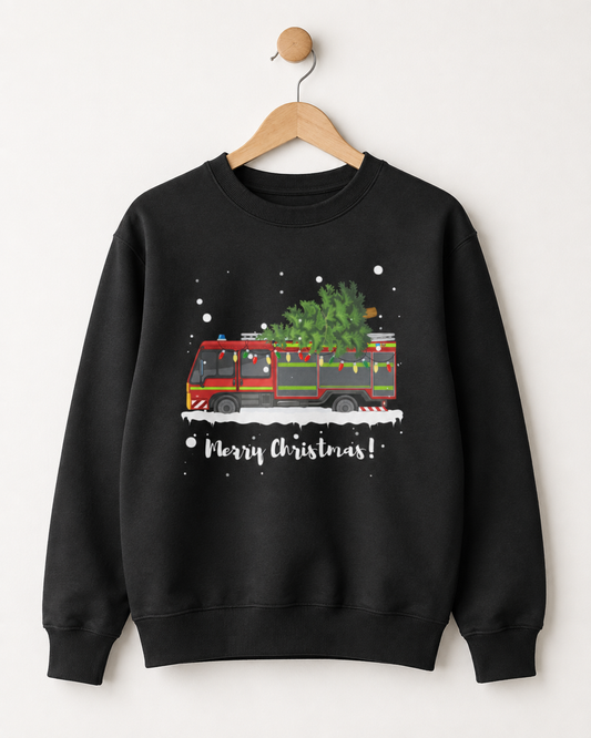 A black crewneck sweatshirt hanging on a wooden hanger against a light beige wall. The sweatshirt features a graphic of a red fire truck carrying a green Christmas tree, with white snowflakes and the text 'Merry Christmas!' printed below.