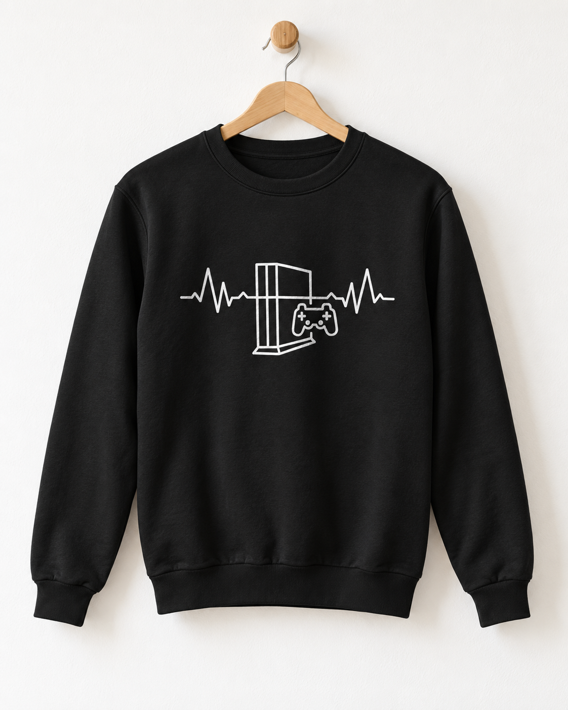 A black crewneck sweatshirt hanging on a wooden hanger against a plain white wall. The sweatshirt features a white line art graphic of a video game console and controller integrated into an EKG heartbeat line across the chest.