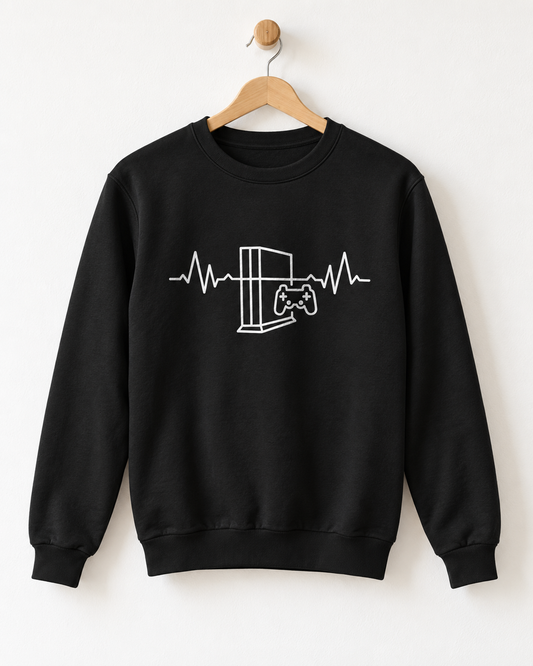 A black crewneck sweatshirt hanging on a wooden hanger against a plain white wall. The sweatshirt features a white line art graphic of a video game console and controller integrated into an EKG heartbeat line across the chest.