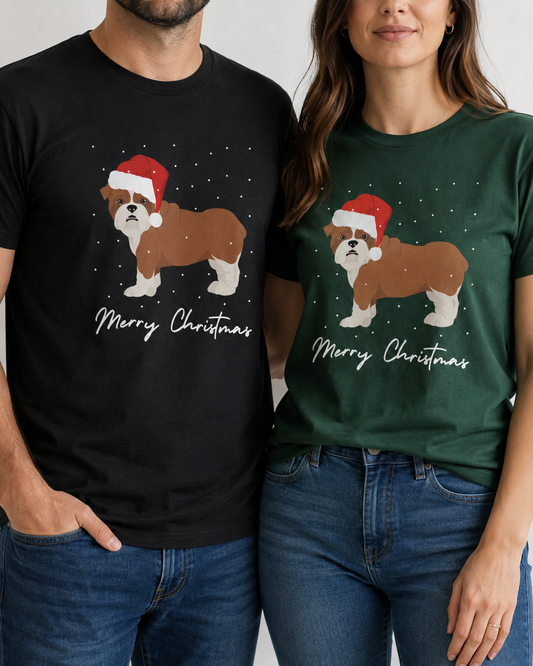 Two models wearing Christmas-themed graphic t-shirts. The model on the left wears a black t-shirt with a brown and white bulldog wearing a Santa hat, and the model on the right wears a dark green t-shirt with the same dog graphic.