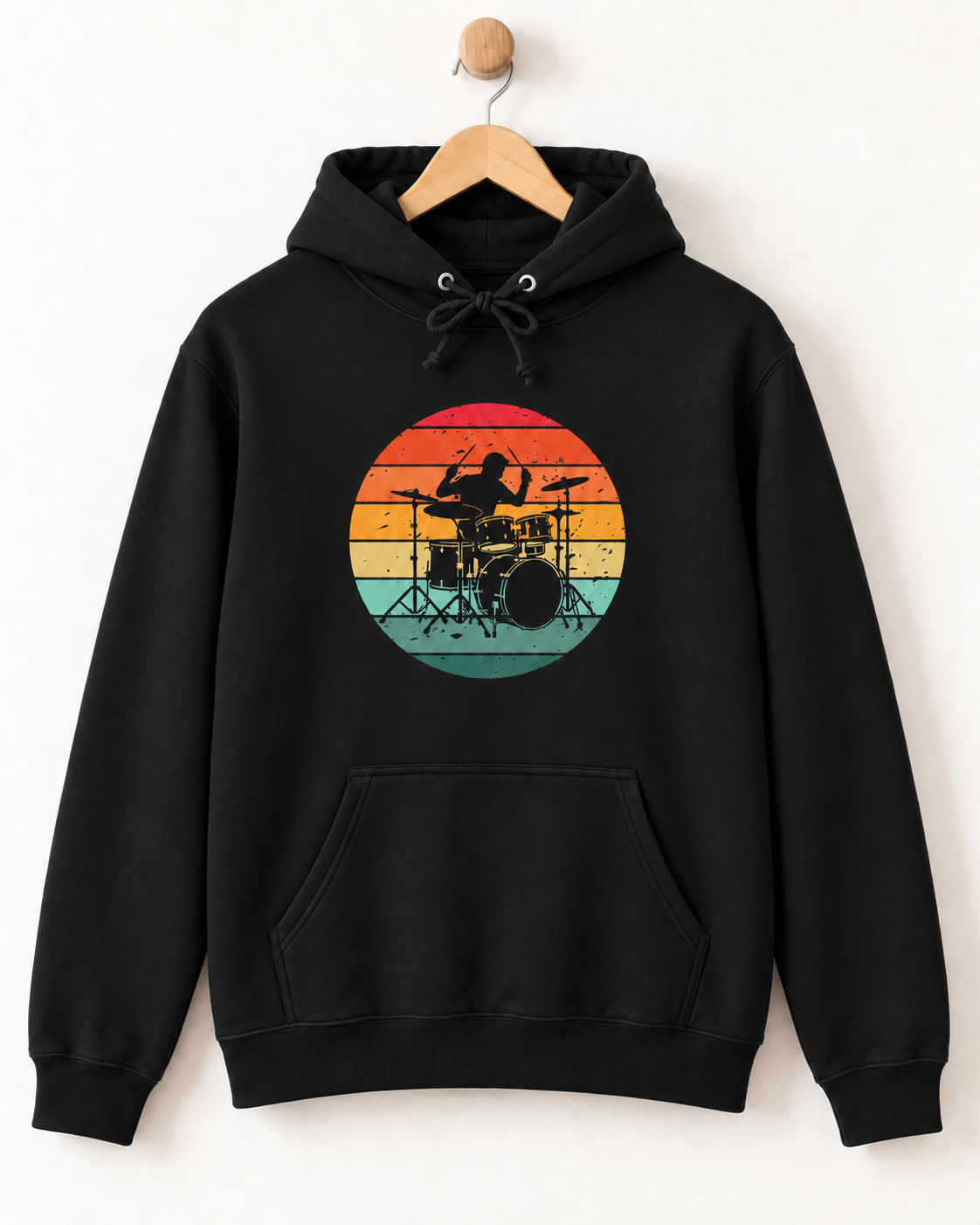 Adults black pullover hoodie hanging on a wooden hanger against a plain white wall. The hoodie features a large circular graphic on the chest showing a drummer in silhouette against a retro sunset gradient of red, orange, yellow, and teal.
