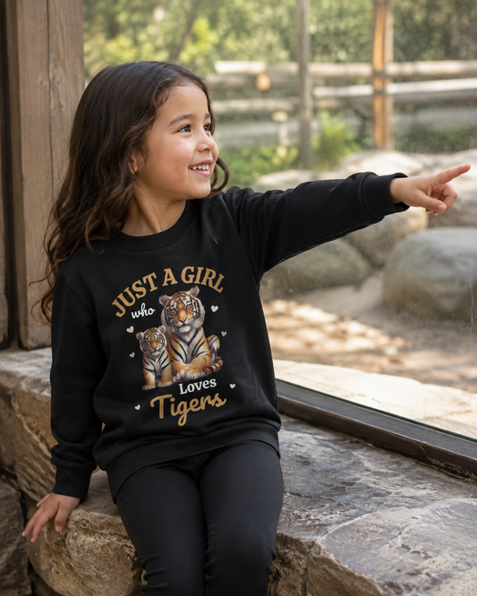 Young girl at the zoo wearing a black tiger sweatshirt with a mother tiger and cub design, smiling and pointing towards an animal enclosure.