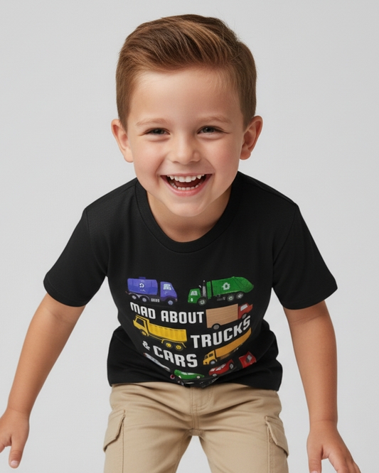 Happy boy leaning forward playfully wearing a black “Mad About Trucks & Cars” kids T-shirt with beige shorts, photographed on a bright white studio background.