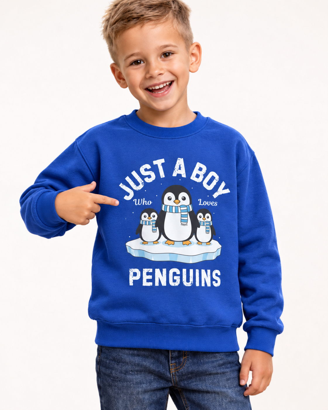Laughing boy pointing to three scarf-wearing penguins on his royal blue “Just a Boy Who Loves Penguins” sweatshirt, paired with denim jeans.