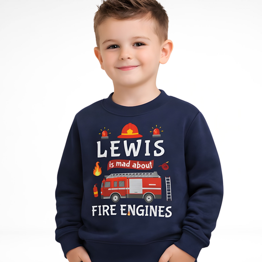 A little boy wearing a black sweatshirt with a fire engine and the text 'LEWIS' is mad about FIRE ENGINES' printed on the front.