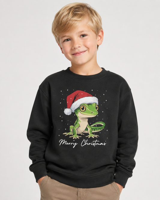 7-year-old blonde boy wearing a black Christmas jumper featuring a green gecko in a Santa hat with Merry Christmas text.