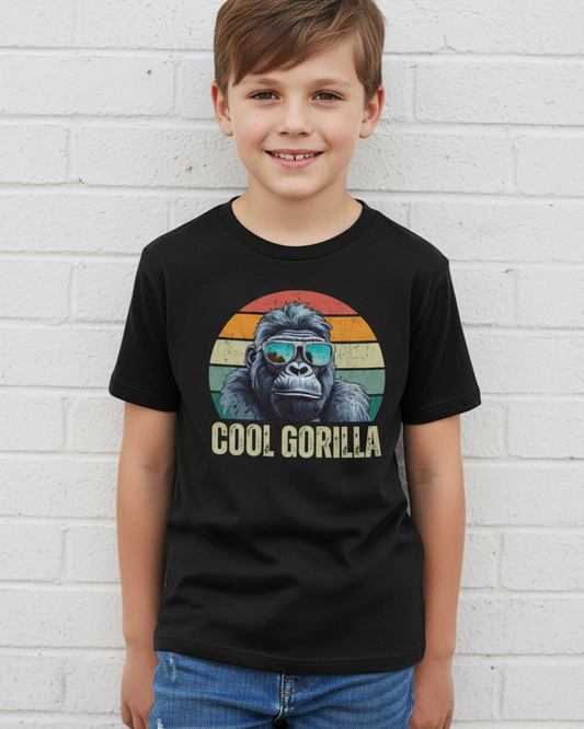 Boy models a black short-sleeve t-shirt with a retro-style graphic of a gorilla wearing blue-tinted sunglasses in front of a distressed sunset circle, with the text 'COOL GORILLA' printed below.