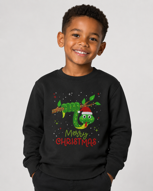 Smiling boy wearing a black kids Christmas jumper with a green festive snake in a Santa hat and “Merry Christmas” text, photographed against a plain studio background.