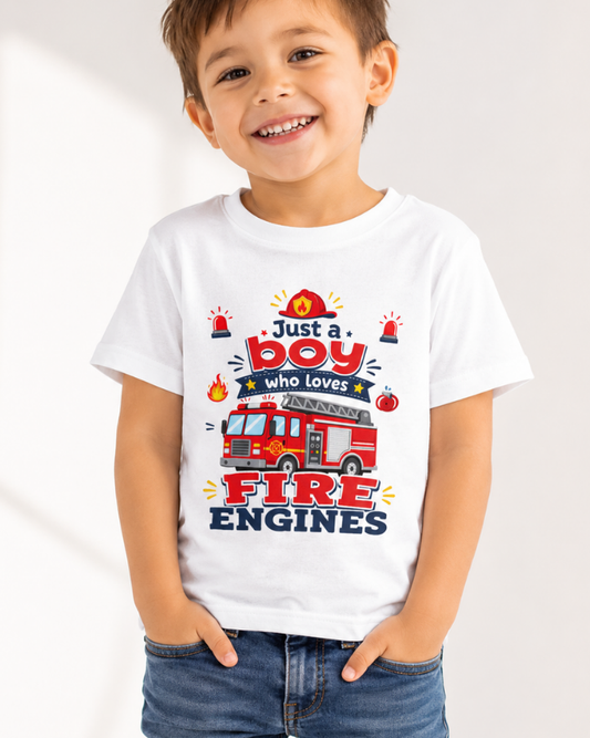 Boy wearing a white kids “Just a Boy Who Loves Fire Engines” T-shirt with a red fire engine graphic and navy shorts in a bright studio setting.