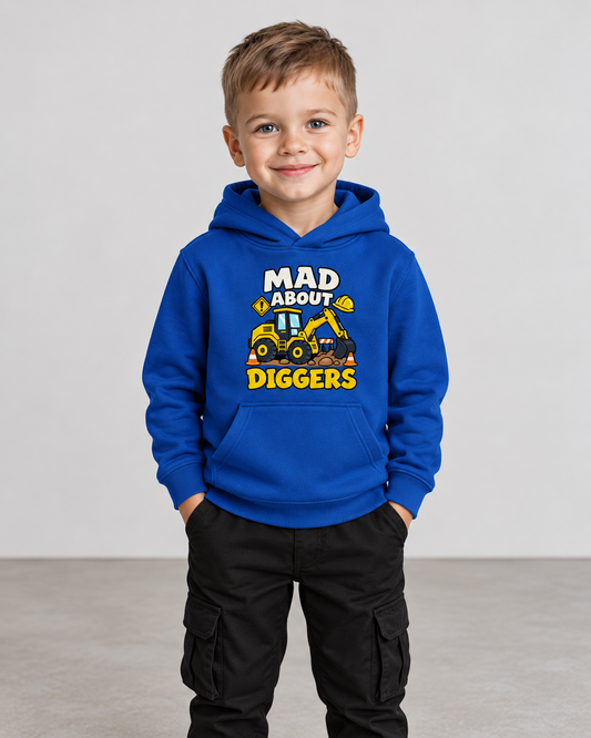A smiling young boy standing with his hands in his pockets, wearing a royal blue kids' pullover hoodie with a "MAD ABOUT DIGGERS" excavator graphic, paired with black cargo trousers.