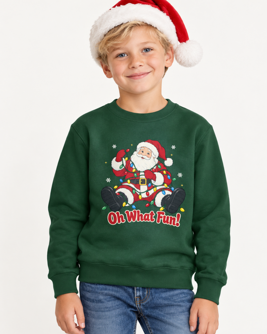 Smiling boy in a Santa hat and jeans wearing a dark green “Oh What Fun!” sweatshirt featuring Santa tangled in colourful Christmas lights.