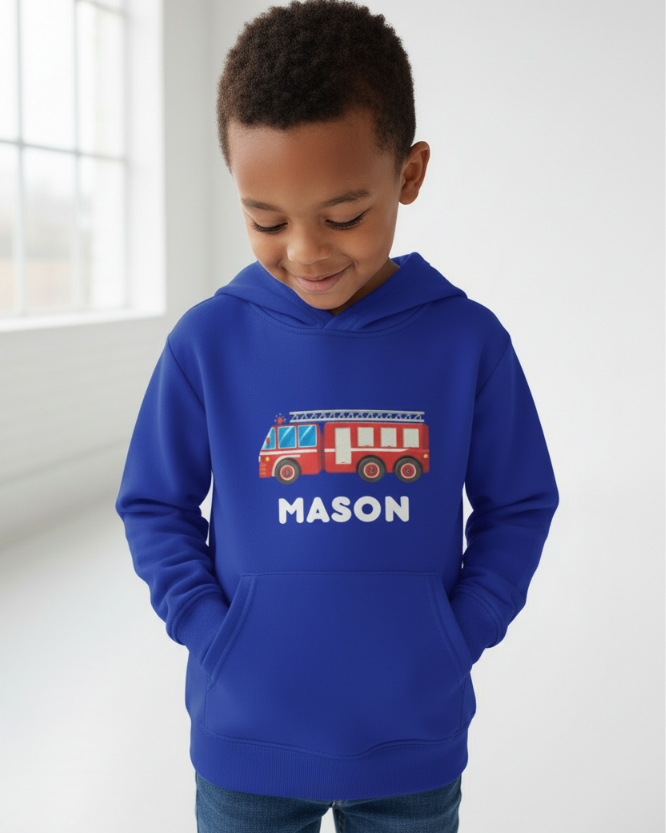 Little boy modelling personalised blue fire engine hoodie with name “Mason”, hands in pocket, soft studio lighting, fire truck graphic clearly displayed.