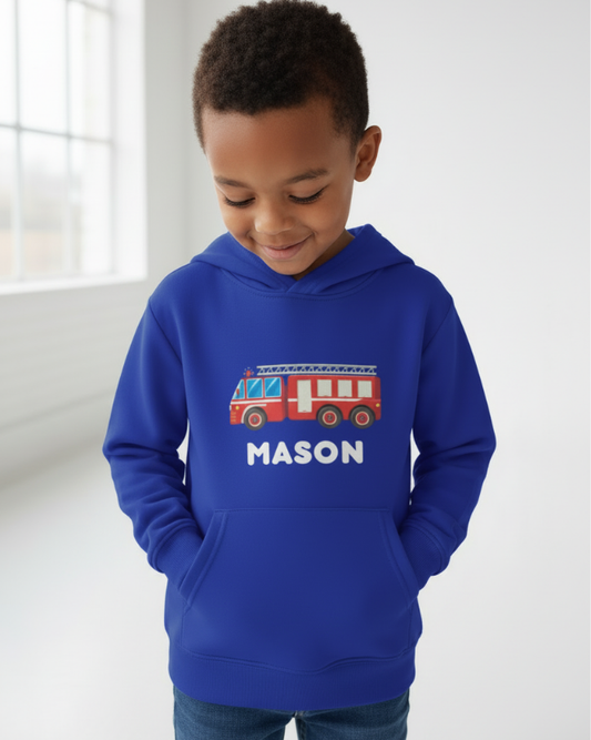Little boy modelling personalised blue fire engine hoodie with name “Mason”, hands in pocket, soft studio lighting, fire truck graphic clearly displayed.