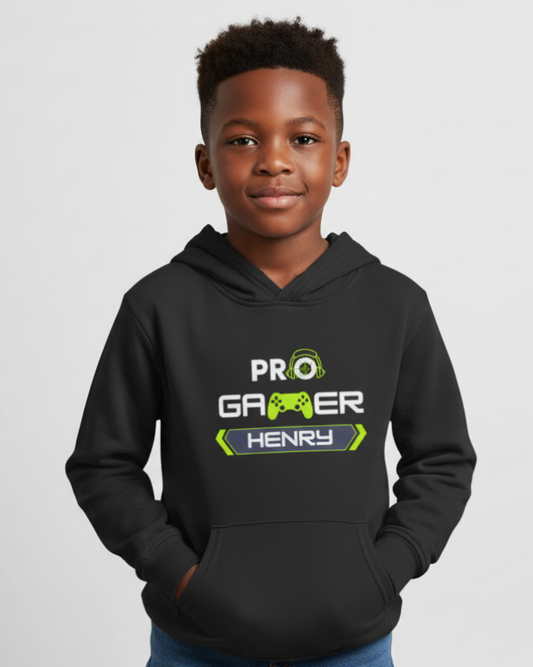 Young boy modelling black kids personalised “PRO Gamer” hoodie with lime green gaming graphic and custom name on chest, hands in pocket, studio background.