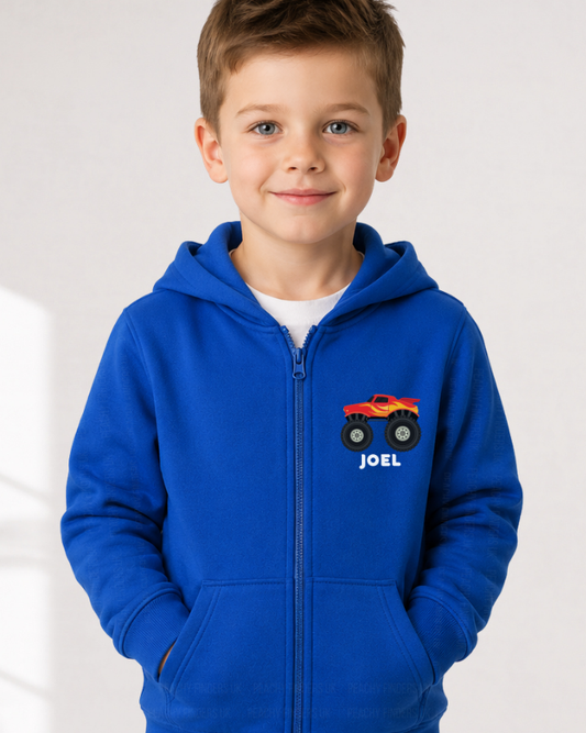 Young boy models a royal blue kids full-zip hoodie featuring a red and yellow monster truck printed on the left chest with the name “Joel” below the design.