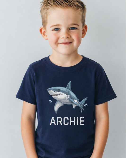 Child wearing a navy blue t-shirt with a shark graphic and 'ARCHIE' text on a light gray background