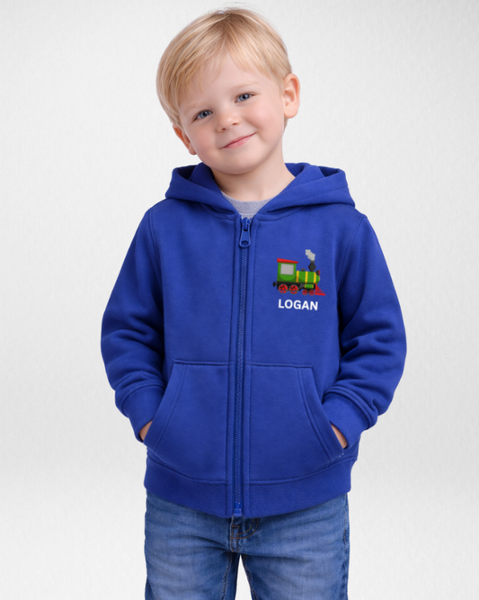 Full-length studio photo of a young boy in a royal blue personalised steam train zip hoodie with name, hands in pockets, wearing jeans.