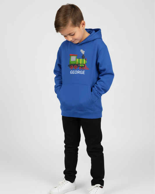 A boy looking downwards models a blue pullover hoodie with a steam train design and custom name 'GEORGE' text on a studio background