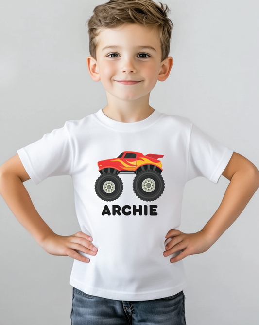 Young boy wearing a white personalised monster truck t-shirt with red flame truck design and name Archie in black text