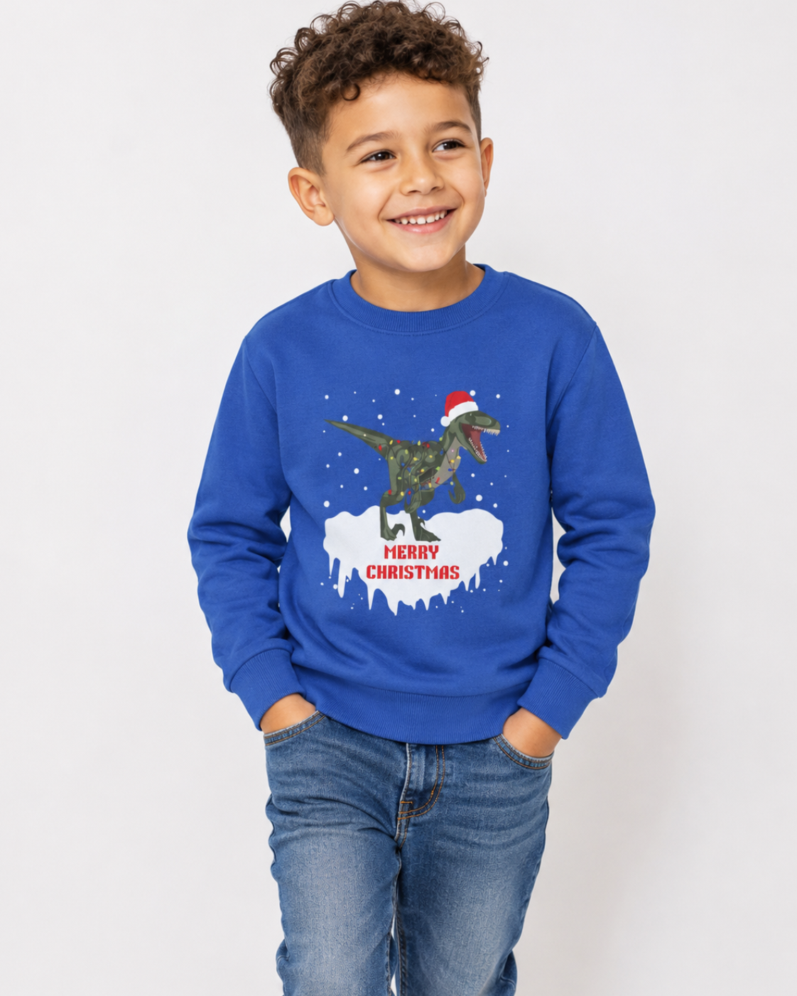 Smiling boy wearing a royal blue T-rex Christmas jumper with Santa hat, festive lights and Merry Christmas design, styled with denim jeans.