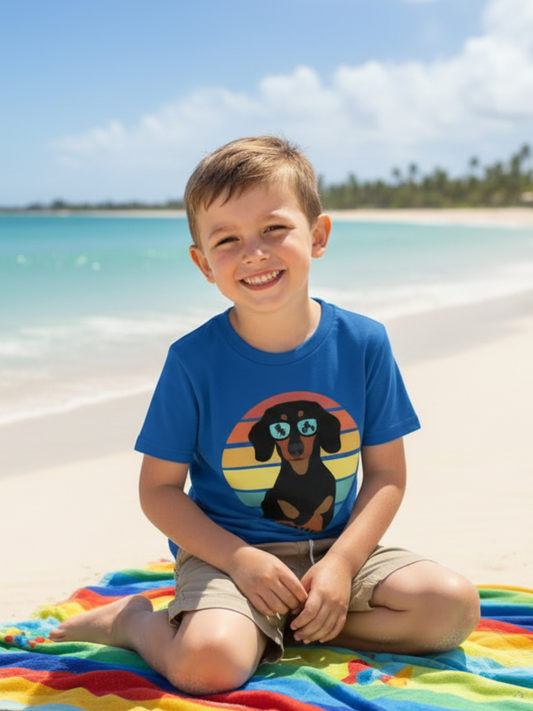 Young boy sitting on a beach towel wearing royal blue retro dachshund graphic t-shirt