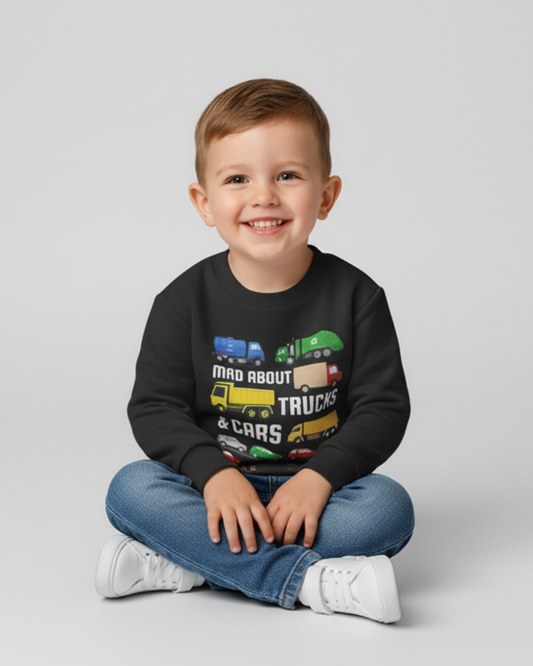 Happy child sitting cross-legged wearing black trucks and cars sweatshirt for kids, colourful transport graphic jumper styled with jeans and white trainers