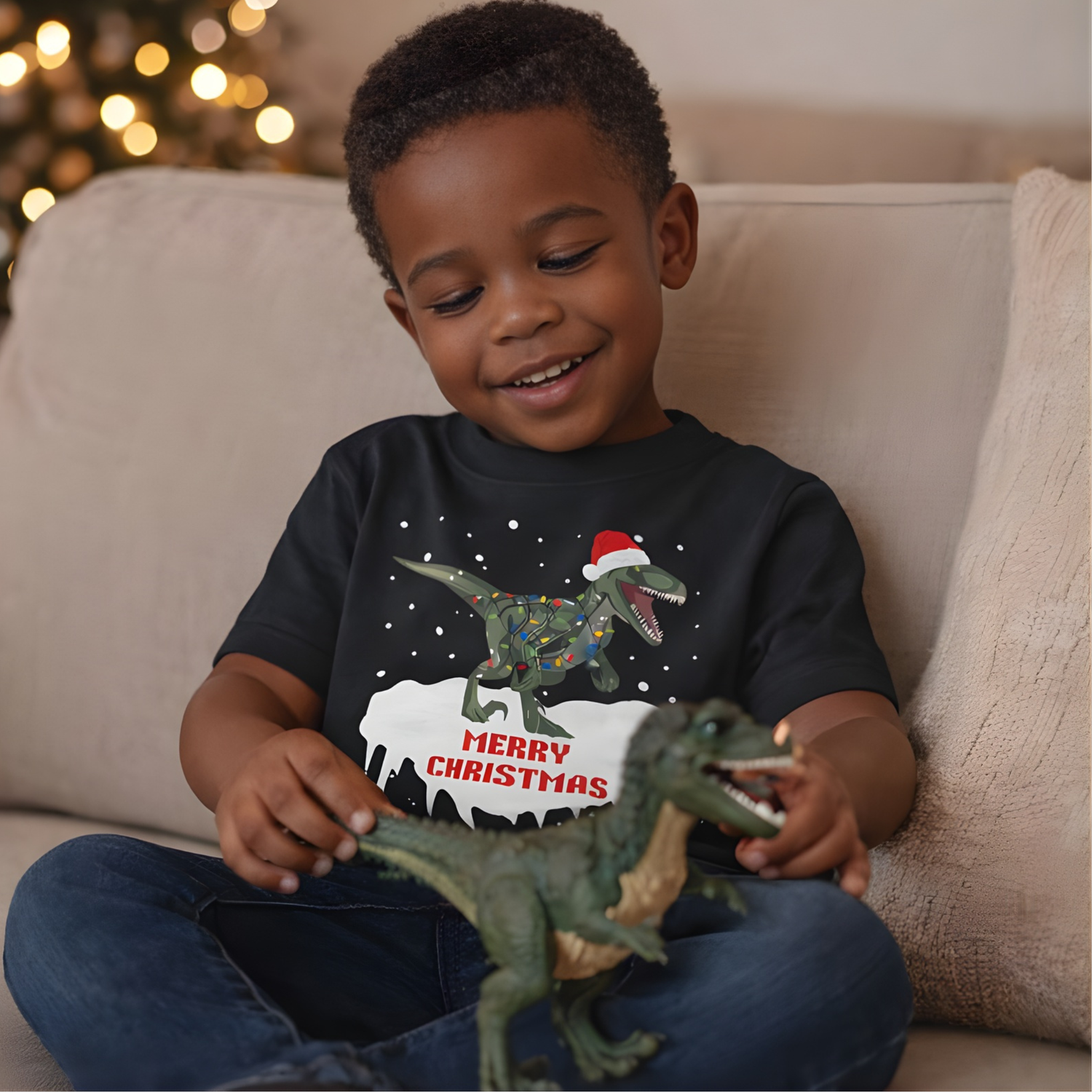 Boy sitting on sofa wearing black kids Christmas T-Rex t-shirt while playing with a dinosaur toy
