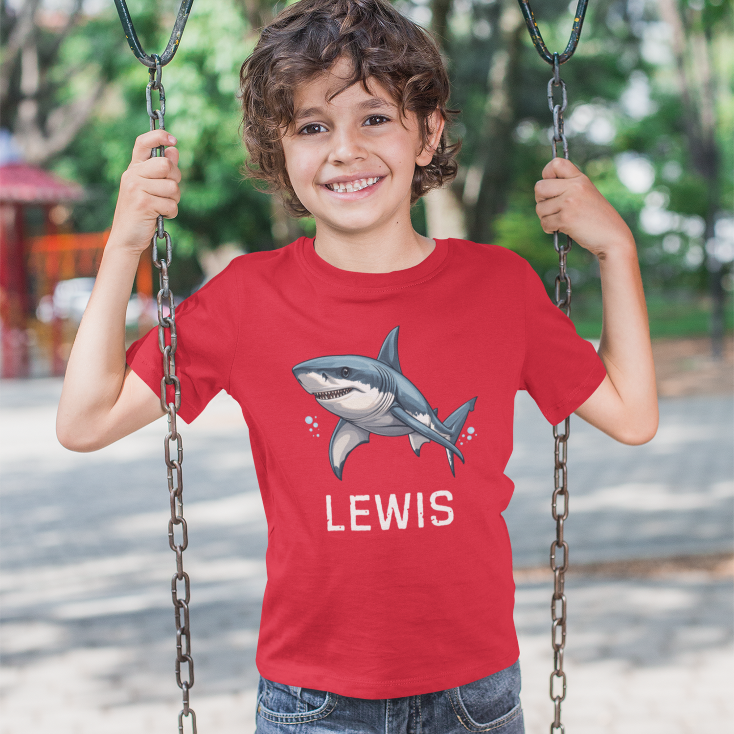 Child wearing a red t-shirt with a shark design and 'LEWIS' text, standing on a swing.