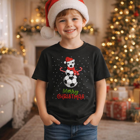 Child wearing a black Christmas-themed t-shirt with a snowman design and 'Merry Christmas' text, standing in a festive room with a Christmas tree and decorations.