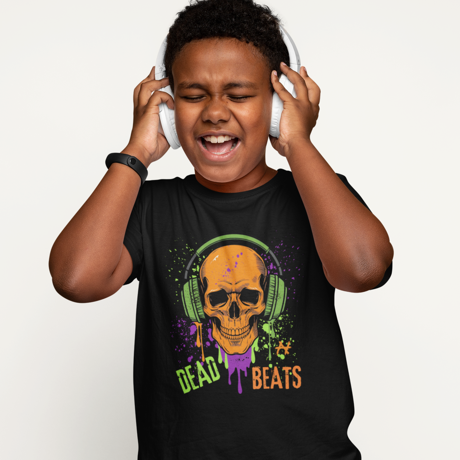 Boy wearing black kids t-shirt featuring orange skull with green headphones and colourful paint splashes reading ‘Dead Beats’