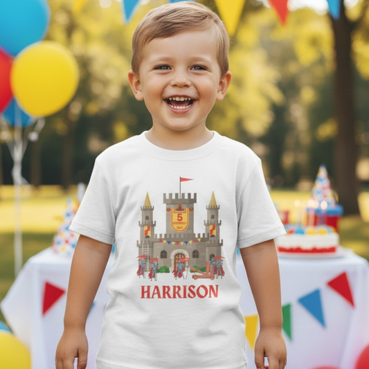 Child wearing a t-shirt with a castle design and 'HARRISON' text, standing outdoors with balloons and a cake.