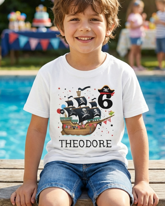 Boy wearing a personalised pirate ship birthday t-shirt with number 6, smiling at a pool party background with balloons.