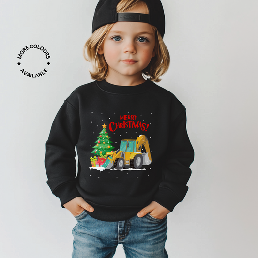 Little boy wearing a black Christmas-themed sweatshirt with a yellow digger/tractor delivering presents and decorated tree design on a plain background.