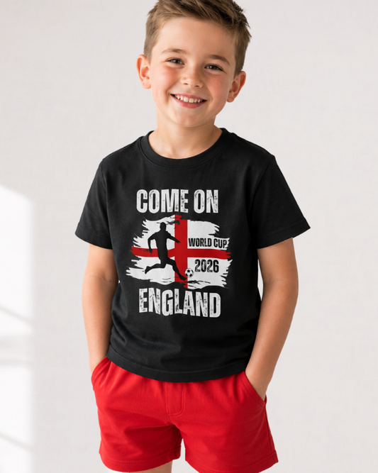 A young boy wearing a black t-shirt. The shirt features a graphic with the text "COME ON ENGLAND," a silhouette of a football player kicking a ball, and the words "WORLD CUP 2026"
