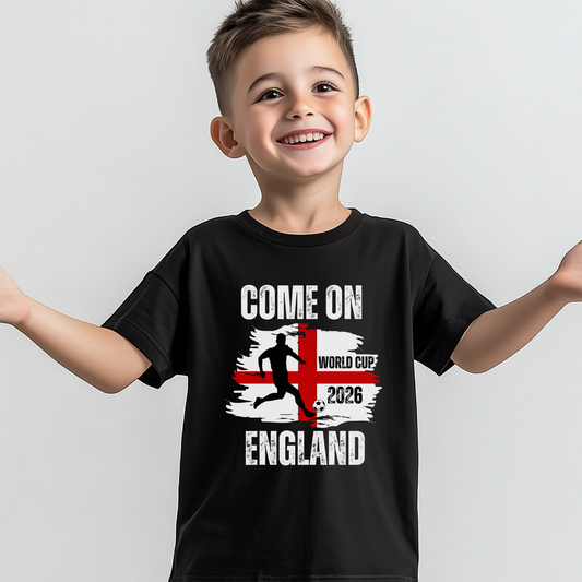 A young boy with short brown hair smiles broadly while wearing a black t-shirt. The shirt features a graphic with the text "COME ON ENGLAND," a silhouette of a football player kicking a ball, and the words "WORLD CUP 2026" over a stylized red and white cross flag.
