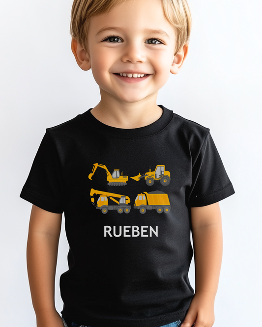 A young boy wearing a black T-shirt with personalised construction vehicles and the name 'Rueben' printed on the front.