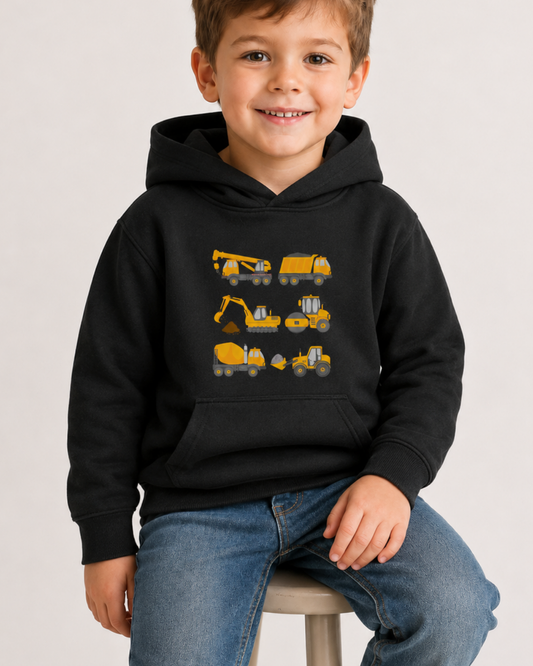A smiling young boy wearing a black pullover hoodie with a graphic print of yellow construction vehicles, sitting on a stool against a light gray background.