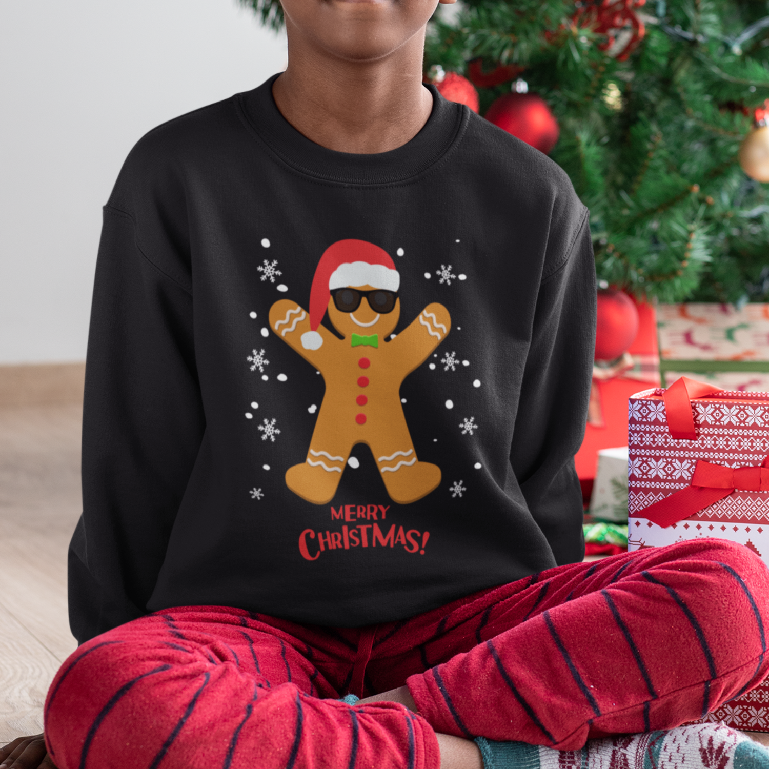 Young boy wears Christmas jumper featuring a cool gingerbread man wearing a Santa hat and sunglasses with snowflakes and “Merry Christmas!” text.