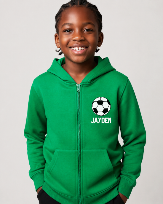 Boy wearing a green personalised football zip hoodie with custom name and football chest design, styled with black joggers in a studio setting.